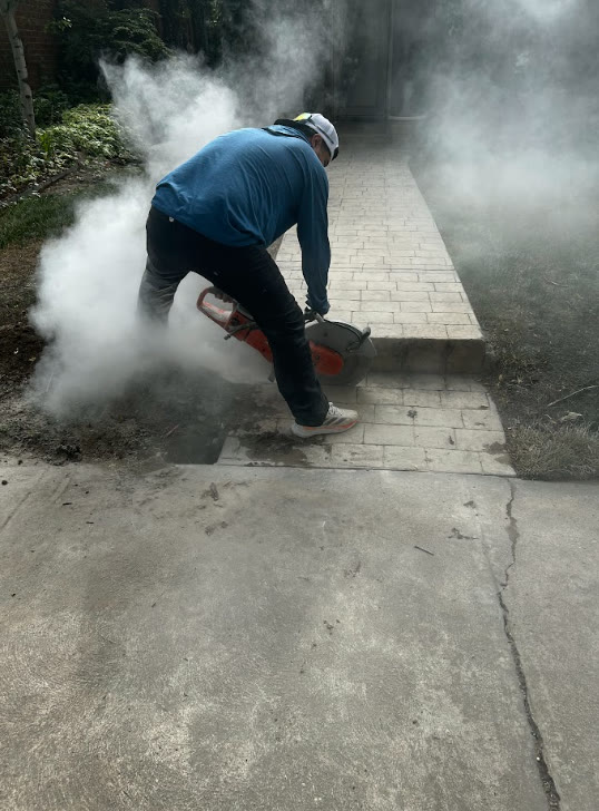 Crew member cutting concrete walkway with a saw