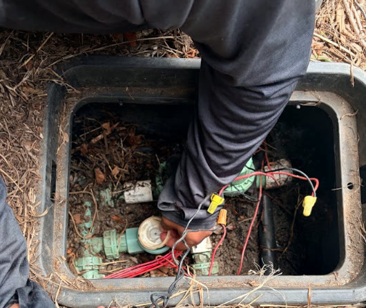Technician servicing sprinkler valves inside a valve box